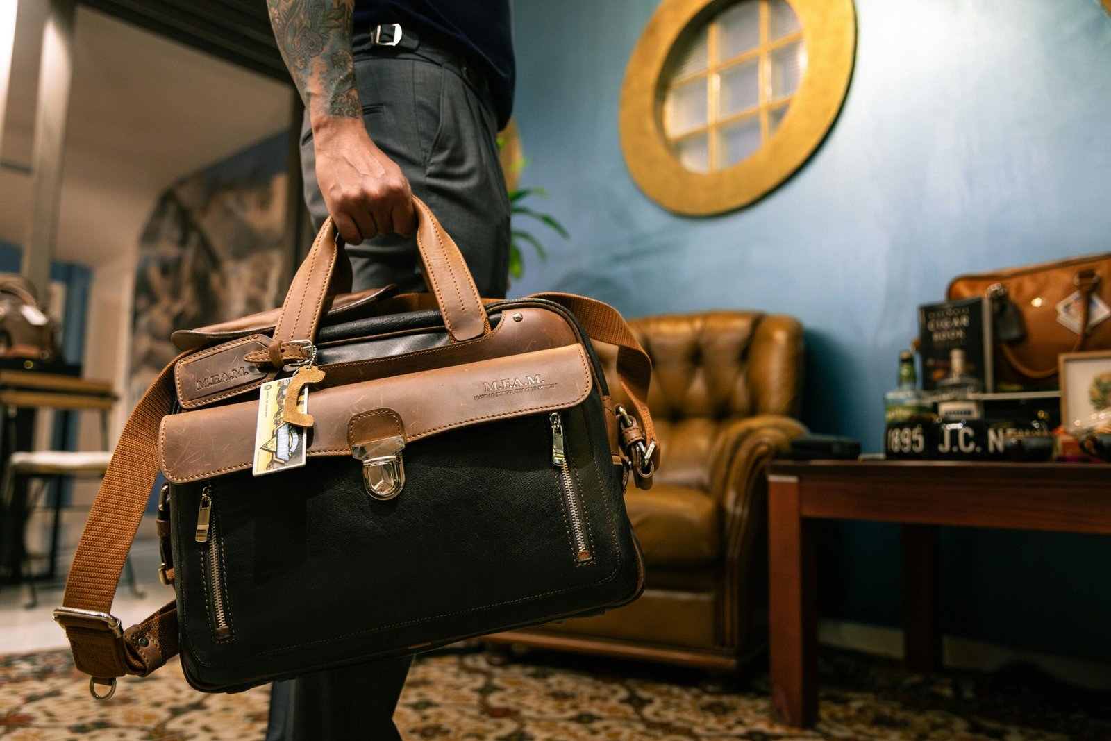 Man holding a brown leather bag in a cozy, stylish indoor setting with vintage decor.